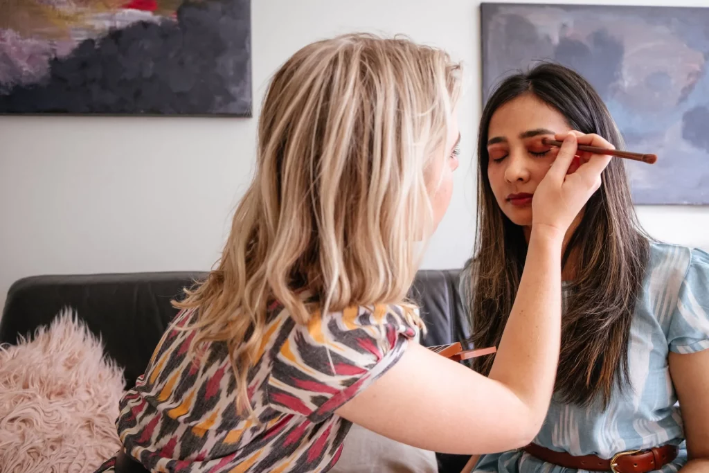One woman is putting makeup on another woman's eyes.